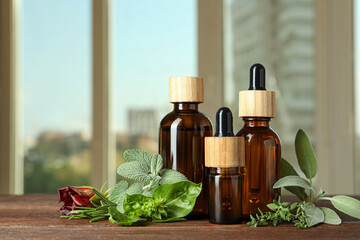 Bottles of essential oil and fresh herbs on wooden table in room. Space for text