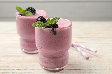 Glasses of blackberry smoothie with mint and berries on light wooden table, closeup