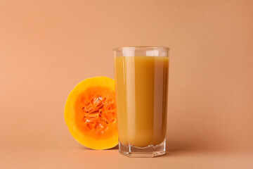 Tasty pumpkin juice in glass and cut pumpkin on pale orange background