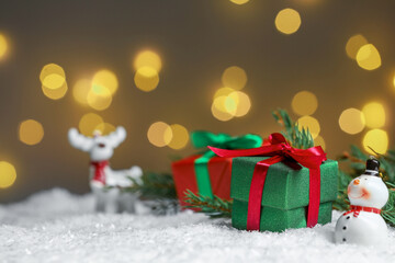 Gift boxes and Christmas decor on artificial snow against blurred festive lights, space for text