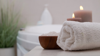 Fototapeta na wymiar Rolled bath towel, sea salt and burning candles on table in bathroom, closeup. Space for text