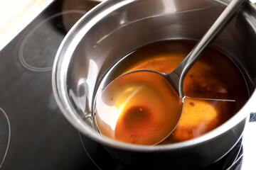 Saucepan and ladle with used cooking oil on stove, closeup