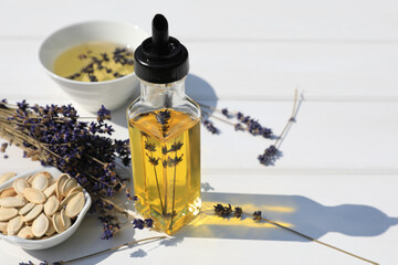 Healthy cooking oil, lavender flowers and pumpkin seeds on white wooden table, closeup. Space for...