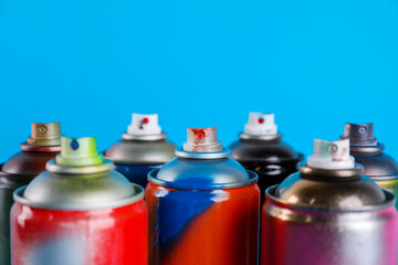 Used cans of spray paints on light blue background, closeup