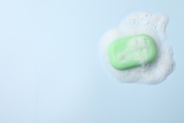 Fototapeta premium Soap and fluffy foam on light blue background, top view. Space for text