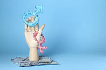 Gender pay gap. Wooden mannequin hand with symbols and dollar banknotes on light blue background,...