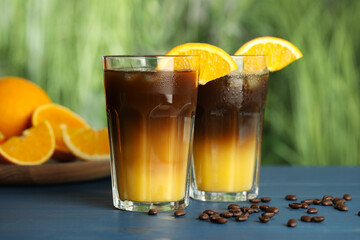 Tasty refreshing drink with coffee and orange juice on blue wooden table against blurred background