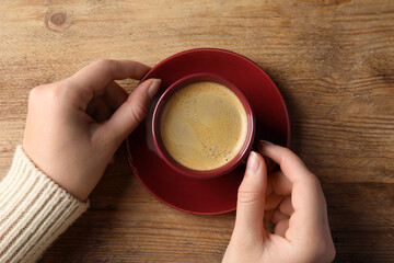 Woman with cup of hot aromatic coffee at wooden table, top view