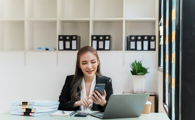 Asian businesswoman in formal suit in office happy and cheerful during using smartphone and working.