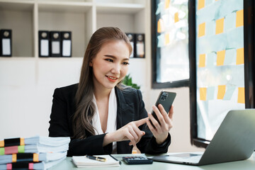Asian businesswoman in formal suit in office happy and cheerful during using smartphone and working.