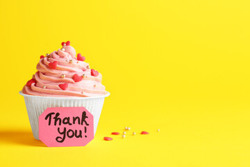 Tasty cupcake and note with phrase Thank You on yellow background, space for text