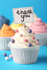 Tasty cupcakes and note with phrase Thank You on light blue background