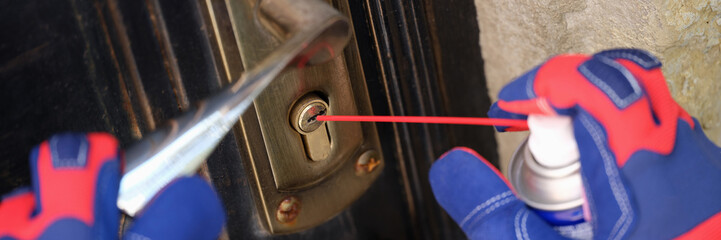 Handyman in gloves pouring penetrating lubricant into door lock closeup