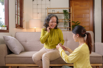 Asian caregiver or daughter takes care of the elderly at home in the living room to squeeze a...