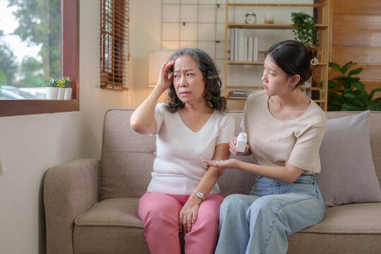 Asian Caregiver Or Daughter Take Care Of The Elderly At Home In The Living Room, Providing Timely Medication.