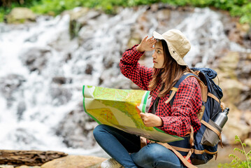 Asian woman in a hat and backpack holding maps