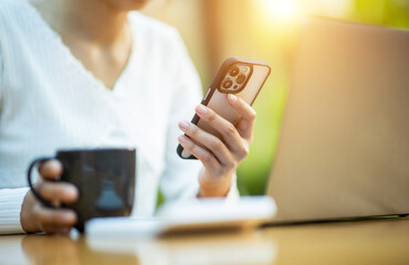 Young woman sitting in a coffee shop at a wooden table Drink coffee and use laptops and smart phones. Young woman surfing the internet, chatting, blogging. Woman holding a cup of coffee in a coffee sh