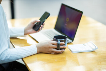Young woman sitting in a coffee shop at a wooden table Drink coffee and use laptops and smart phones. Young woman surfing the internet, chatting, blogging. Woman holding a cup of coffee in a coffee sh