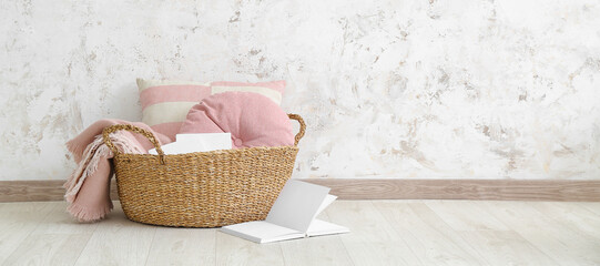 Fototapeta na wymiar Wicker basket with pillows, plaid and books in room