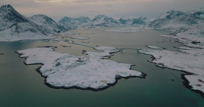 Wintry lake bridge between Ramberg village on snowy Lofoten Nordland glacial island aerial orbiting view