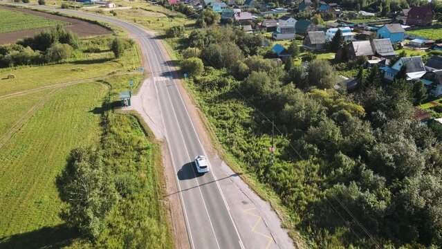 Aerial shot of a white car driving down an empty rural road.