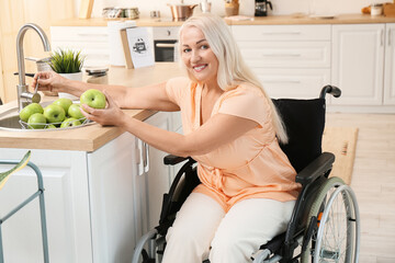 Mature woman with physical disability washing apples in kitchen
