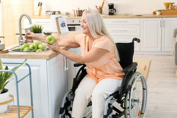 Mature woman with physical disability washing apples in kitchen