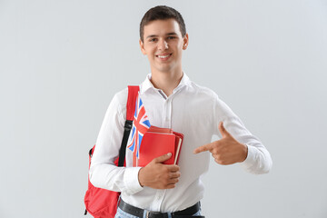 Teenage boy with UK flag and backpack pointing at books on light background