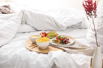 Board with tasty breakfast on white blanket in bedroom