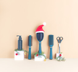 Set of various hairdressing tools, hair comb in red Santa hat, fir branches and Christmas balls on a beige background, front view, copy space.