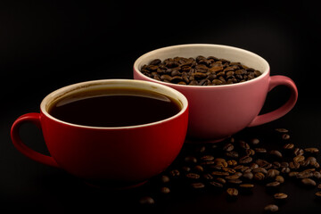 Coffee in red cup and coffee beans in a pink cup on black background.