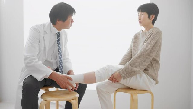 医者に包帯を巻かれる中年女性　医療イメージ