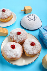 Plate with tasty donuts and Jewish hat for Hanukkah celebration on blue background, closeup