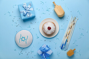 Plate with doughnut, candles, Jewish hat, dreidels and gifts for Hanukkah celebration on blue background