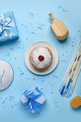 Plate with doughnut, candles, dreidels and gifts for Hanukkah celebration on blue background