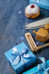 Tasty doughnut with dreidels, candles, rattle and gifts for Hannukah celebration on blue wooden background
