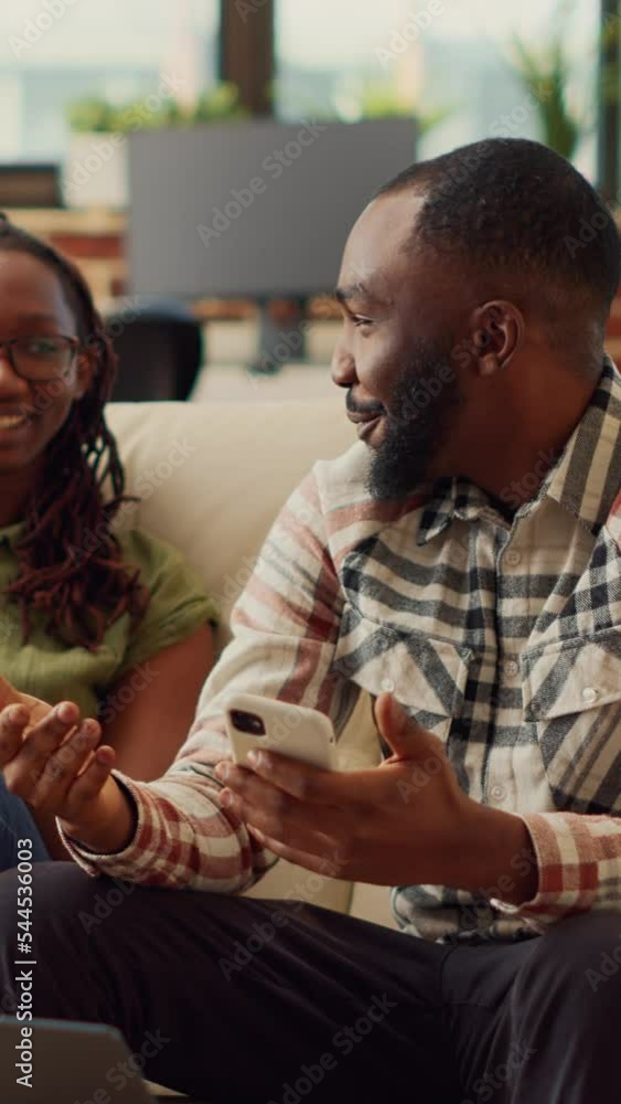 Poster vertical video: young partners using mobile pohnes together on couch, browsing internet and scrollin