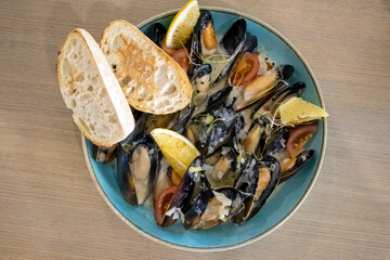 Cooked baked mussels in sauce with lemon and croutons on a blue plate top view