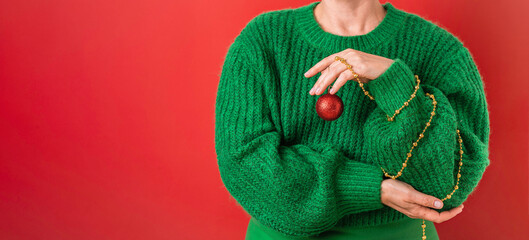 Women in a green sweater holding symbol of the New Year in her hands - a red Christmas ball....