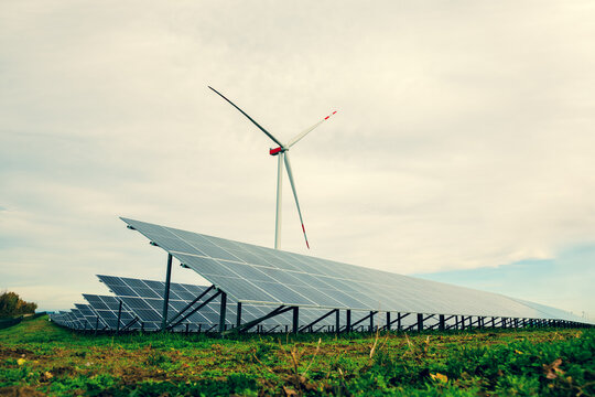 Solar panels and a wind turbine in a field. Solar power station in a moody landscape scenery