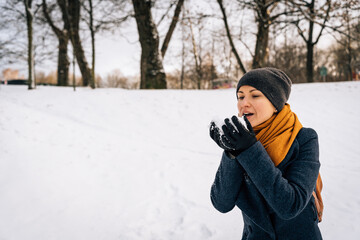 A woman blows snow off her palms in winter