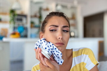 Portrait of young woman suffering from toothache, cooling her face with a ice pack - obrazy, fototapety, plakaty