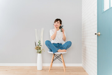 Fototapeta na wymiar 椅子に座りながら化粧品・コスメで保湿する日本人女性 