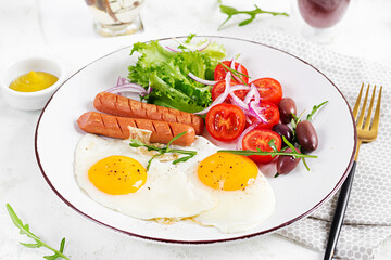 English breakfast - fried eggs, sausages, tomatoes and olives. American food.