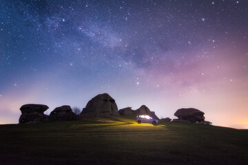 A car with a light inside stands near the ancient stone remains under the the milky way. Sanctuary on Big Allaki Lake.