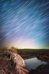 Star trails in the night sky above the rocky cliff and Chusovaya river