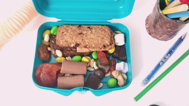 School kids lunch box sweet snacks. Blue container healthy break meal oat cookies biscuits, chocolate dragee, peanuts nuts bar, fruit gummies. Sugar candies children's school packed food video
