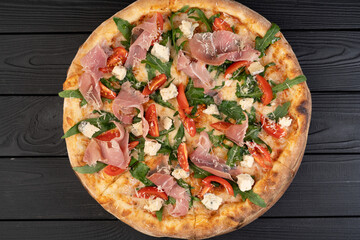 Italian cuisine concept. Pizza with prosciutto, arugula and parmesan on wooden background, top view.