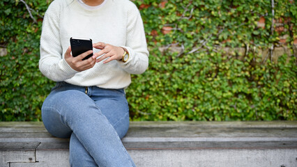 Fototapeta premium Close up view of young female using smartphone in the park while sitting