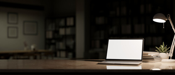 Workspace with laptop mockup, light from table lamp and copy space over blurred dark living room